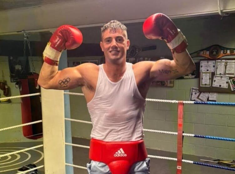 A boxer in red gloves and a white vest raising both arms in the club ring.